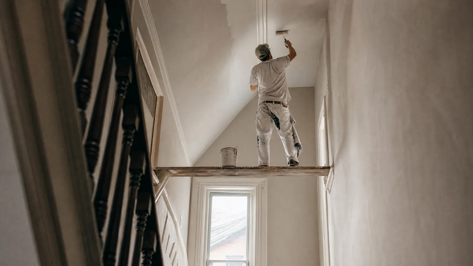 Painter rolling a fresh white finish across a living room ceiling in a Toronto home with the floor fully covered