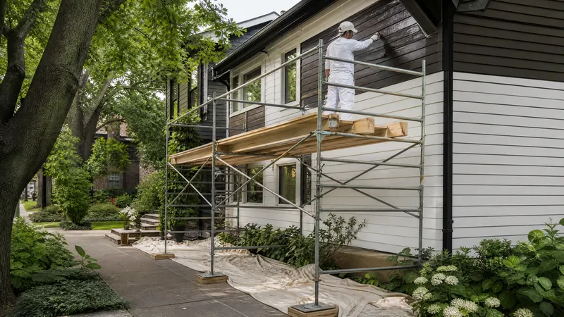 Painter on a ladder coating the wood siding and fascia of a two storey Toronto house